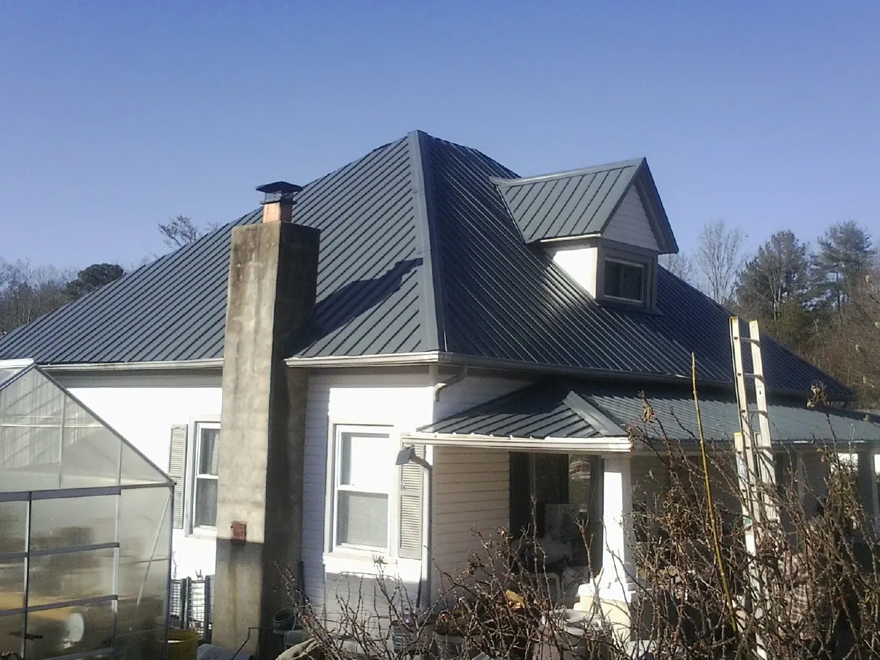 Dark blue standing seam metal roof on a white farmhouse with dormer in Blanch