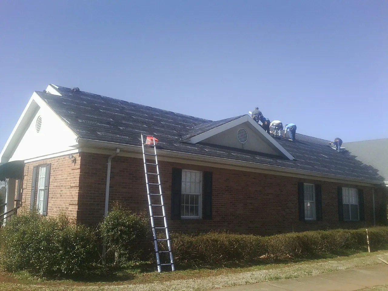 Crew tearing shingles off a brick ranch roof with a ladder set — Metal Roof Repair work by our crew in Blanch