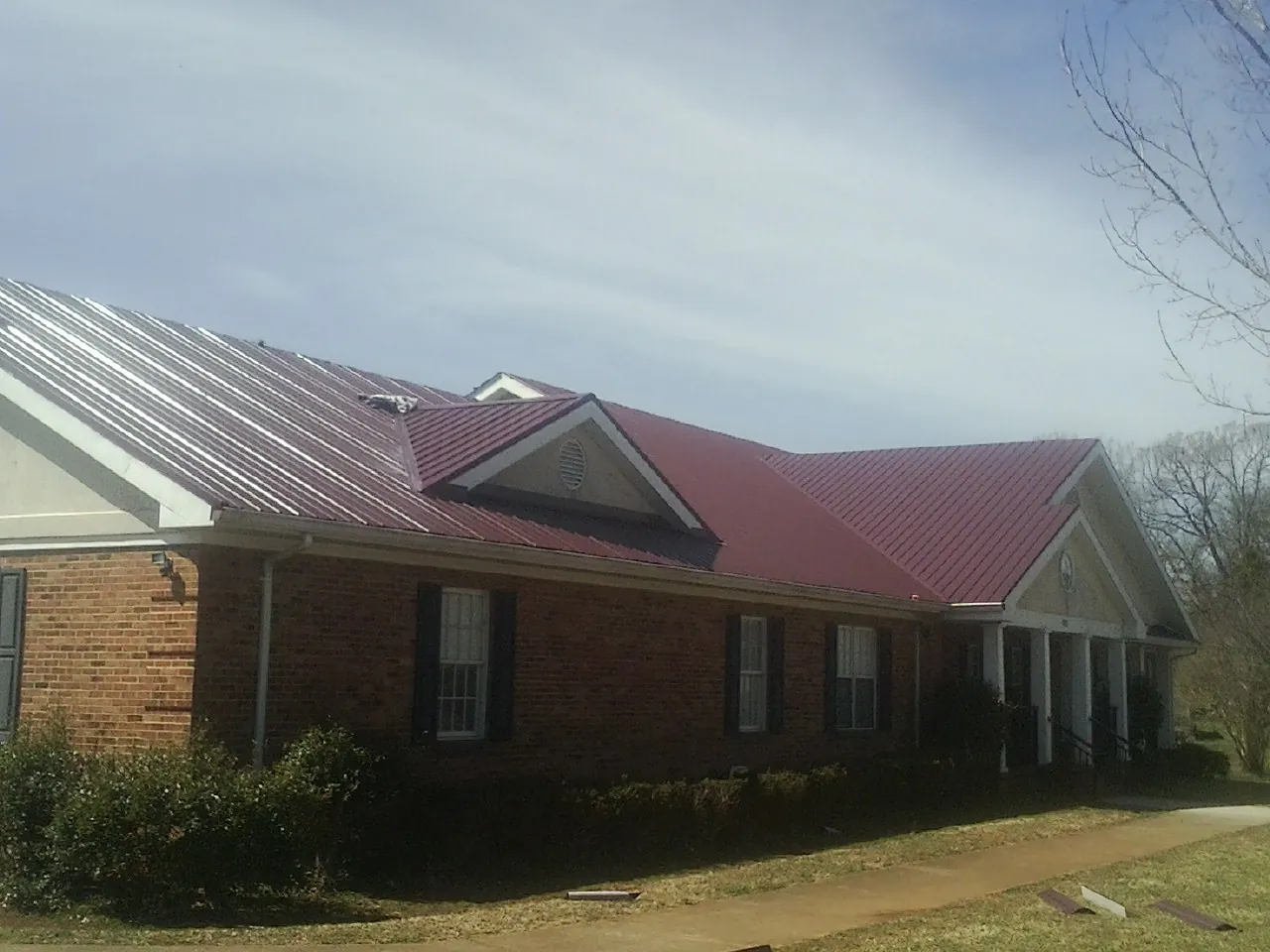 Red metal roof with gabled entries on a long brick building, from a Hail Damage Roof Repair job in Blanch