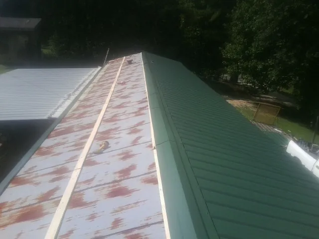 Old rusted panels beside newly installed green metal roofing — Wind Damage Roof Repair by Roofing Brothers in Blanch