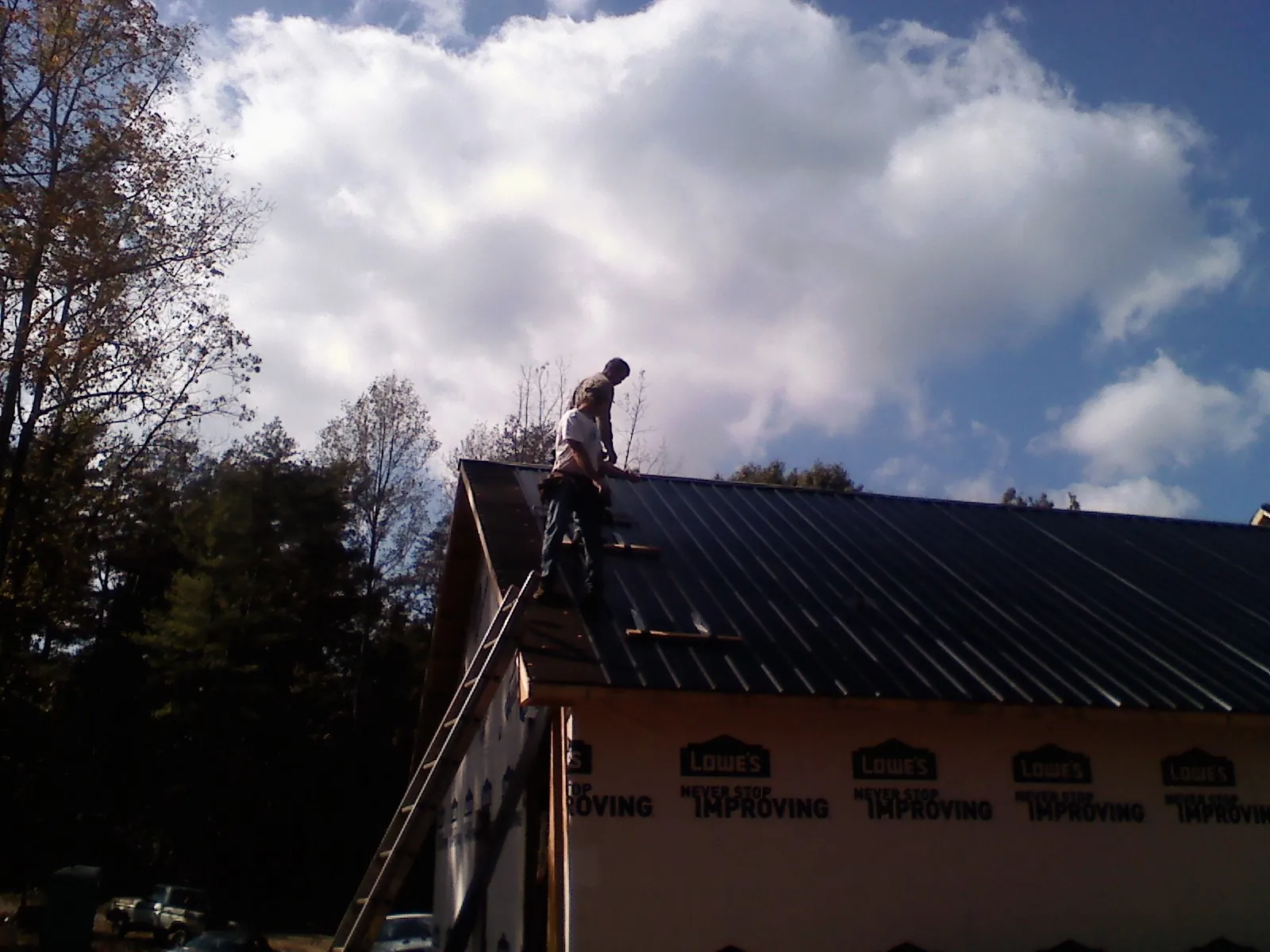 Roofer fastening dark metal panels high against a cloudy sky, from a Roof Inspection job in Blanch